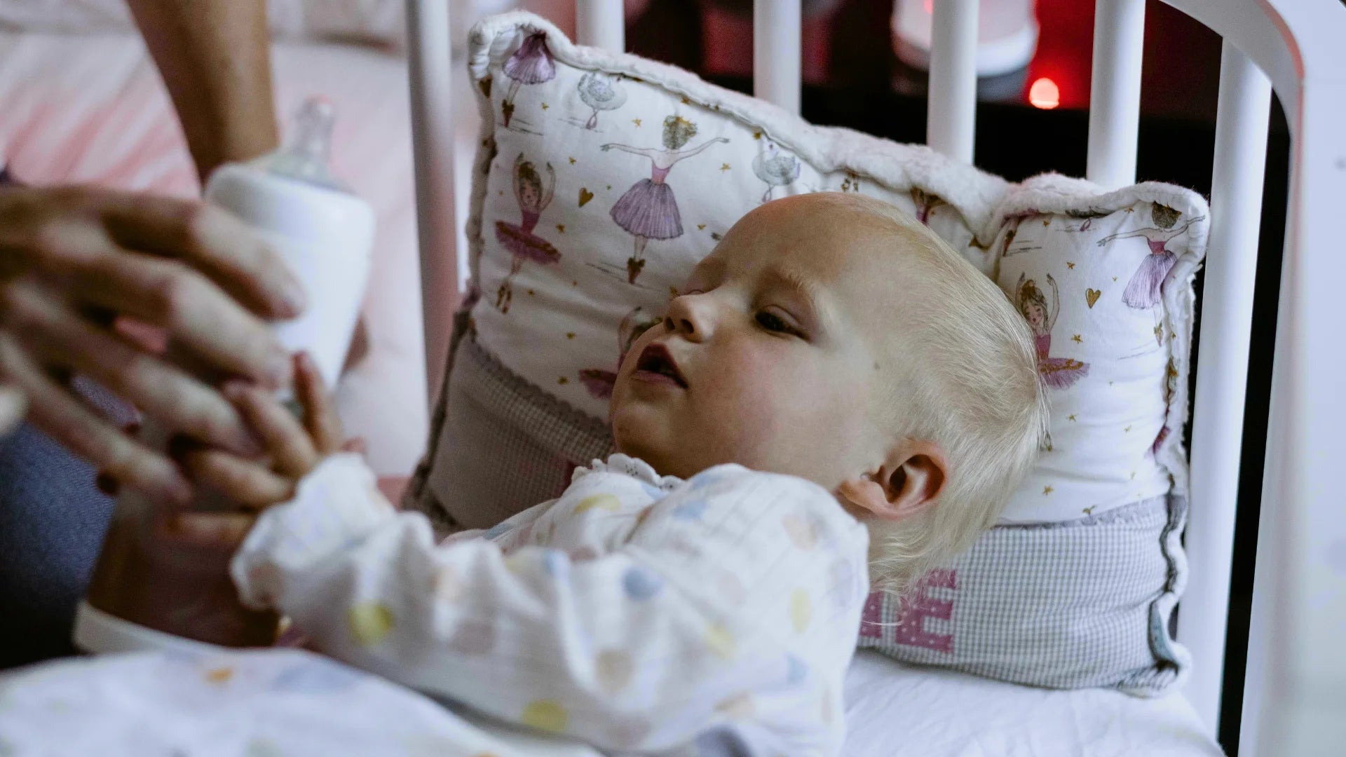 Baby (1 Jahr alt) liegt im Gitterbett am Elternbett und bekommt die snoozi Nachtflasche gereicht