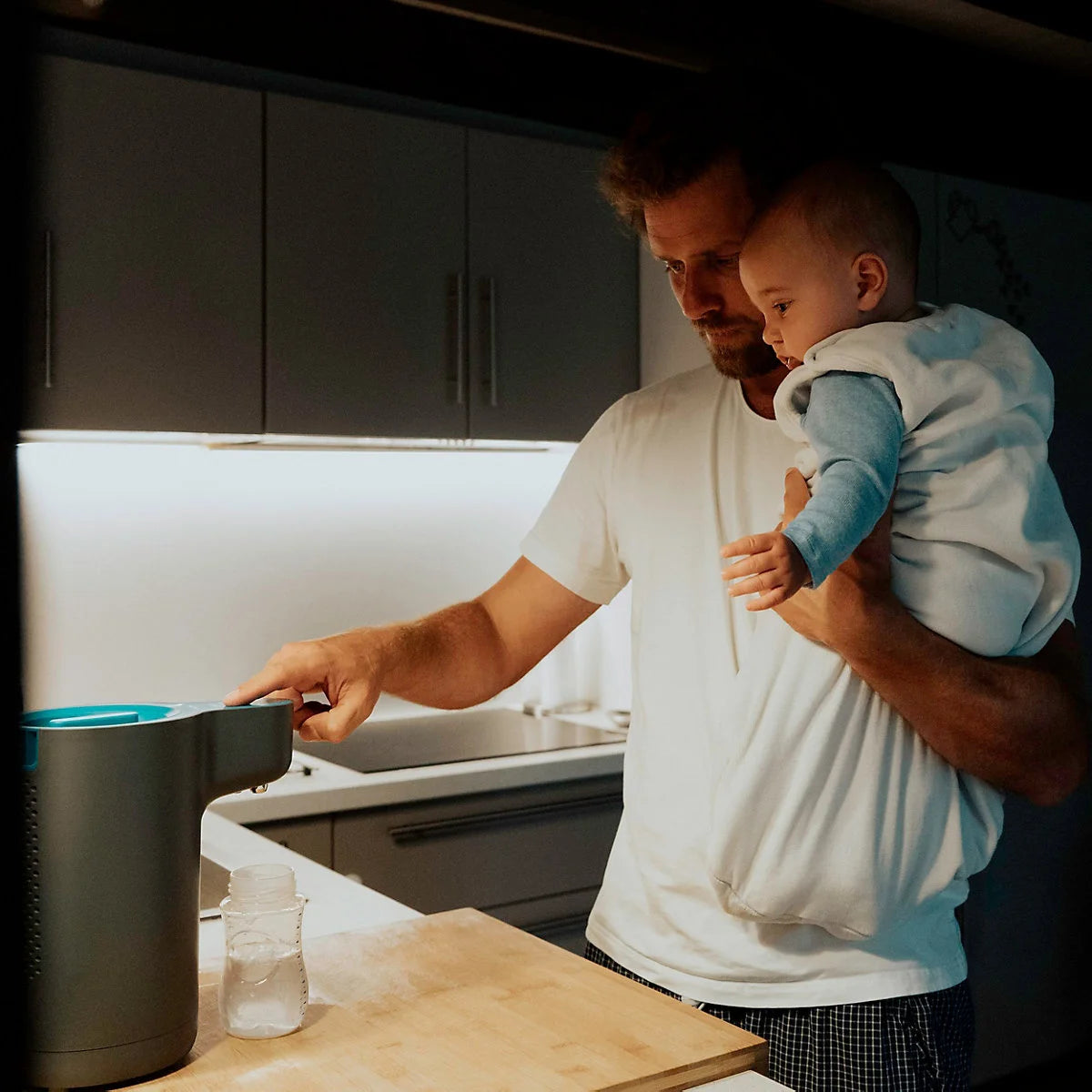 Vater mit Baby bereitet in der Nacht die Babyflasche mit einem Flaschenzubereiter in der Küche vor