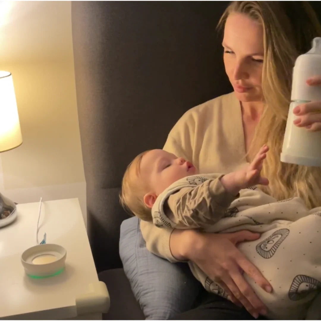 Mutter die Baby mit der snoozi Nachtflasche füttert. Flasche wird vom Flaschenwärmer genommen, auf den Knopf gedrückt und Milchpulver fällt in Wasser 